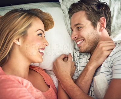 Buy stock photo Shot of a happy young couple lying face to face with each other in bed