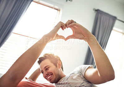 Buy stock photo Shot of a young couple making a heart shape with their fingers in the bedroom