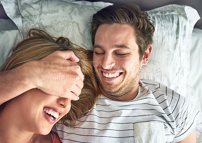 Buy stock photo Shot of a young man playfully covering his girlfriend’s eyes while lying in bed