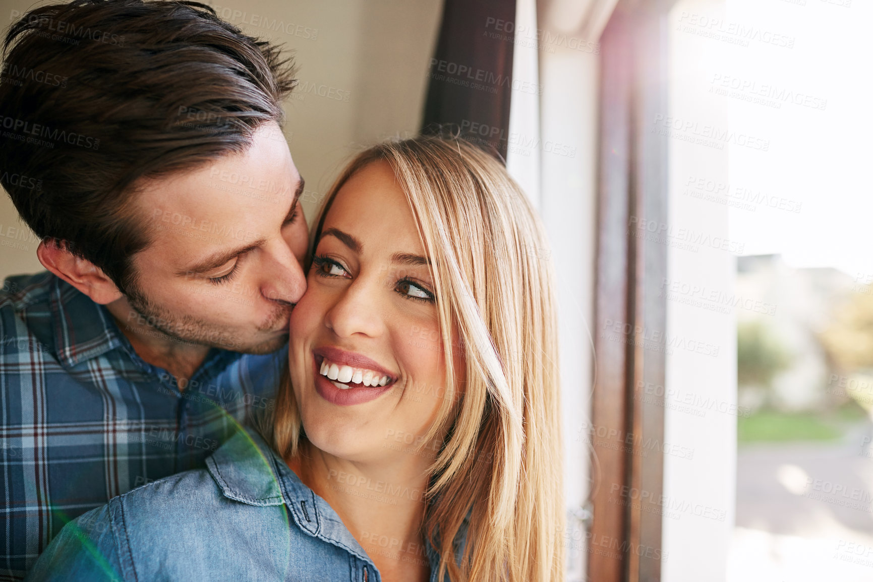 Buy stock photo Cropped shot of an affectionate young couple standing at a window in their home