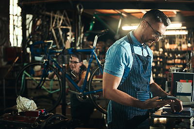 Buy stock photo Shot of a mature man using a calculator in a bicycle repair shop with his coworker in the background