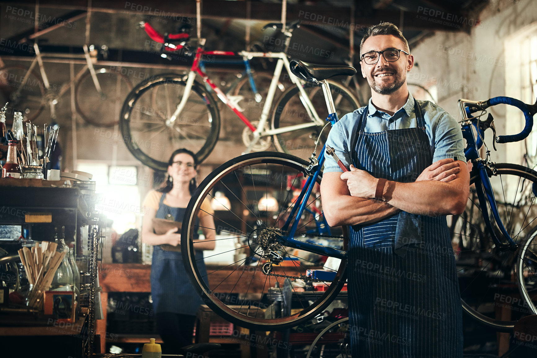 Buy stock photo Portrait of a mature man working in a bicycle repair shop with his coworker in the background