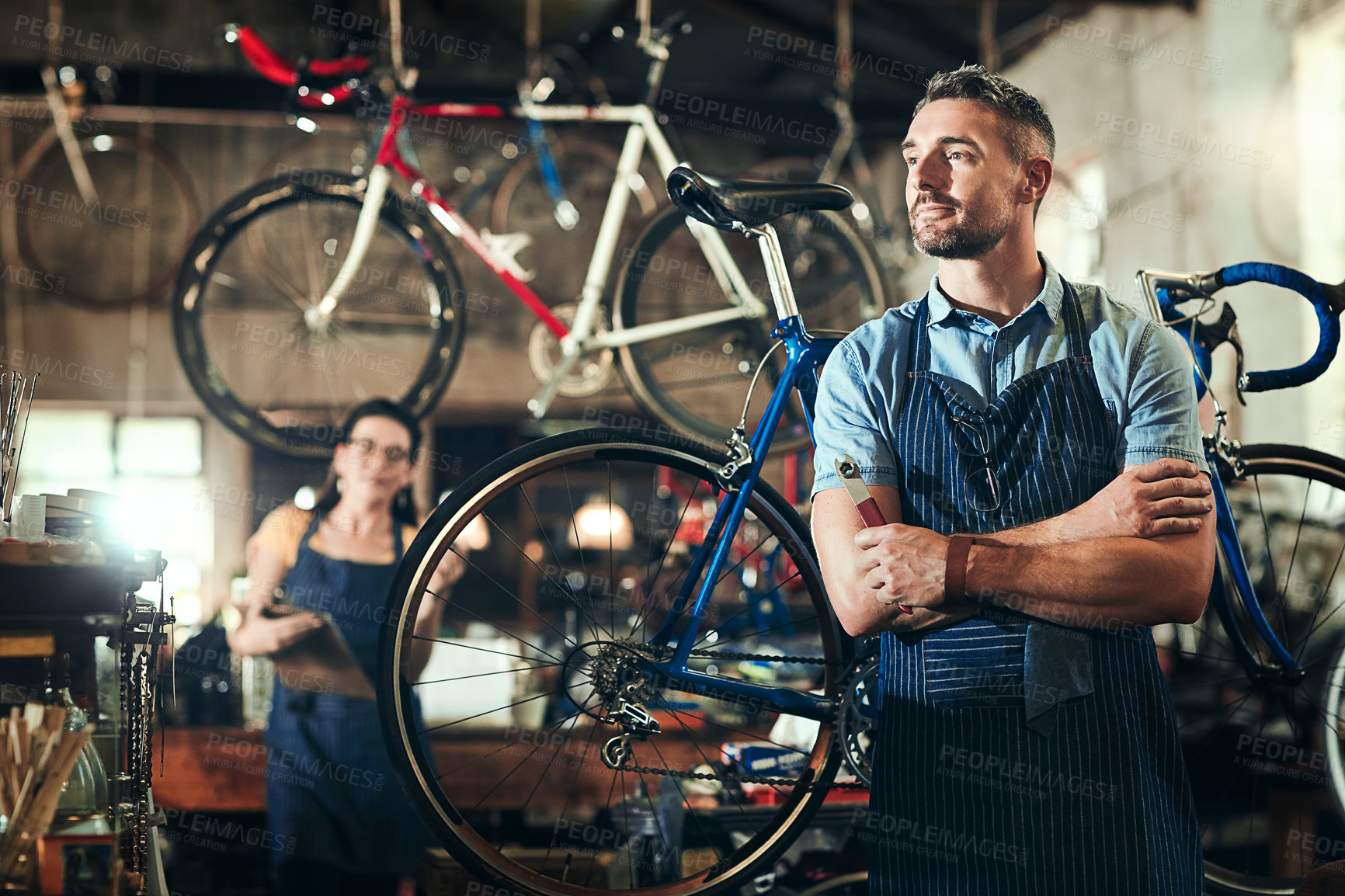 Buy stock photo Shot of a mature man working in a bicycle repair shop with his coworker in the background