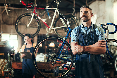 Buy stock photo Shot of a mature man working in a bicycle repair shop with his coworker in the background
