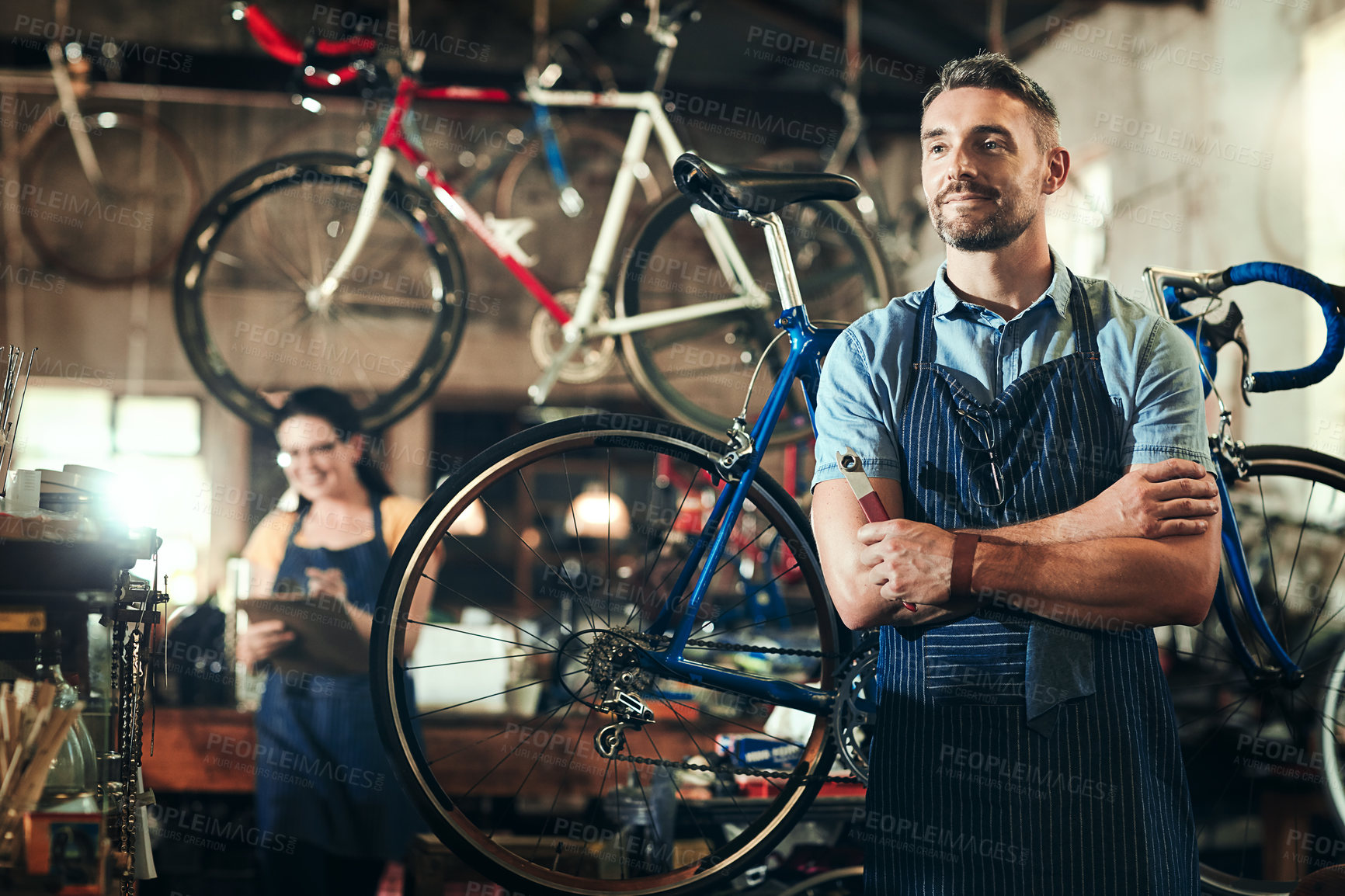 Buy stock photo Shot of a mature man working in a bicycle repair shop with his coworker in the background