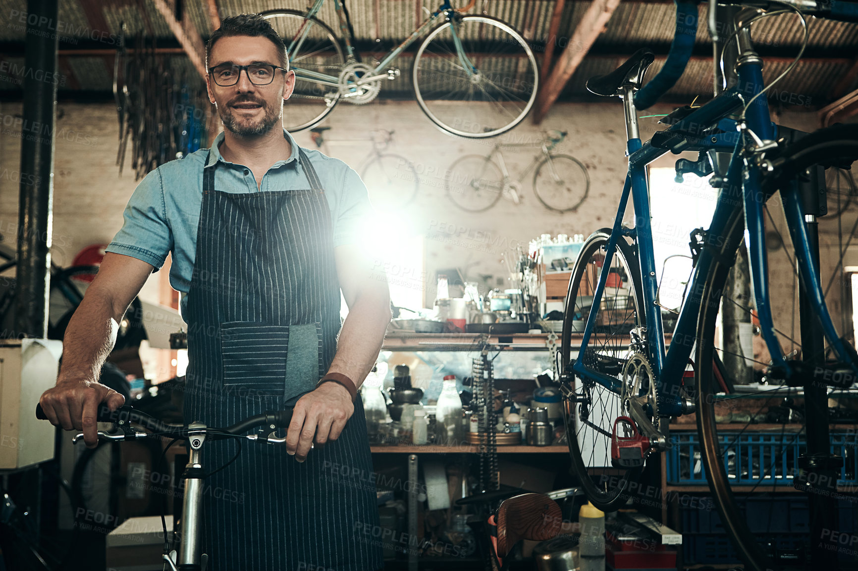 Buy stock photo Man, bicycle shop and portrait for maintenance work, startup with transport service. Bike, mechanic and Male entrepreneur in workshop with glasses, happiness for sustainable business with apron