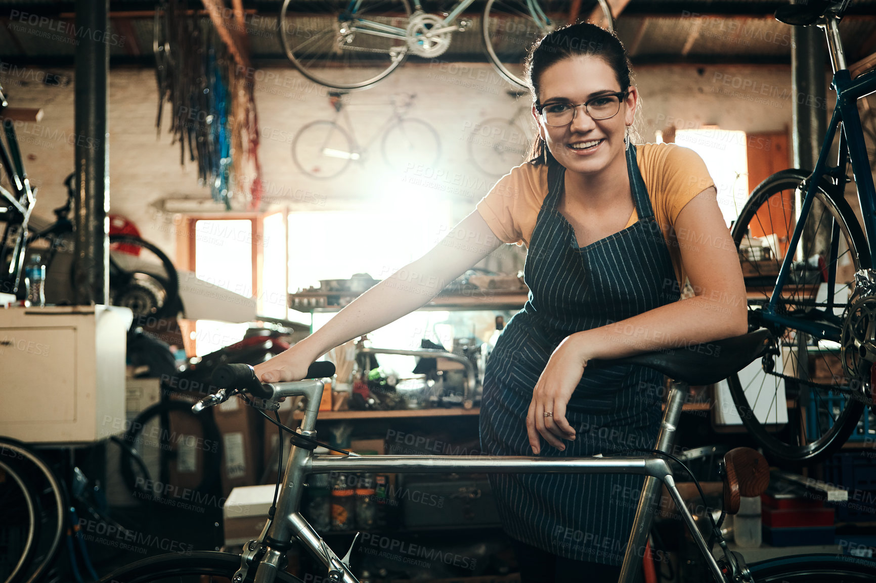 Buy stock photo Woman, bicycle shop and portrait for maintenance work, startup with transport service. Bike, mechanic and female entrepreneur in workshop with glasses, happiness for sustainable business with apron