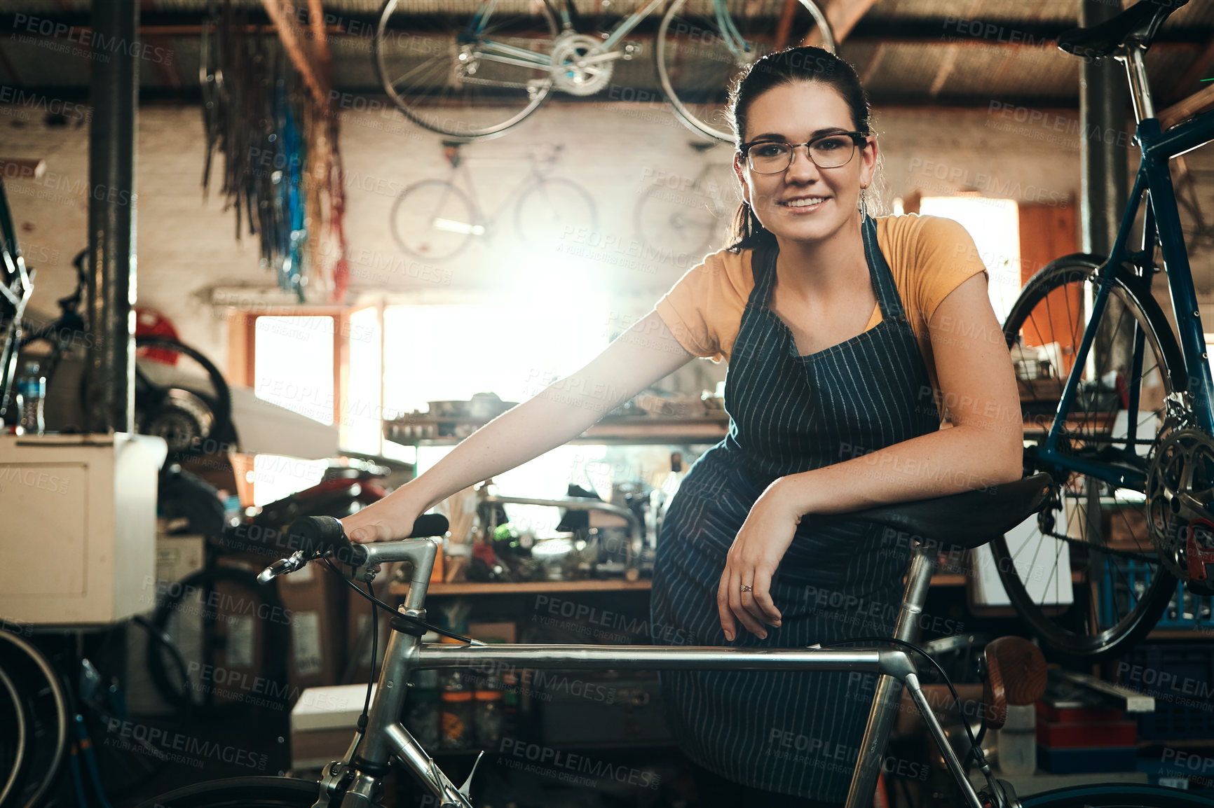 Buy stock photo Woman, bicycle shop and portrait for maintenance job, startup with transport service. Bike, mechanic and female entrepreneur in workshop with glasses, happiness for sustainable business with apron