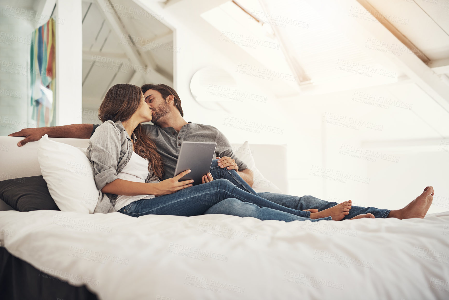 Buy stock photo Happy, kiss and couple in bedroom on tablet for bonding, loving relationship and relax together. Marriage, home and man and woman on digital tech for online videos, streaming and watching movies