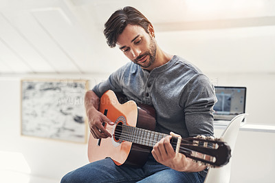 Buy stock photo Shot of a handsome young man practising guitar at home