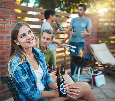 Buy stock photo Shot of a thoughtful and happy young woman enjoying a beer at a barbecue with her friends
