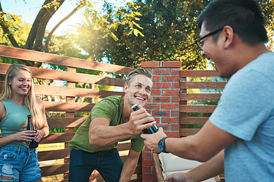 Buy stock photo Shot of a happy young man passing his friend a beer while hanging out