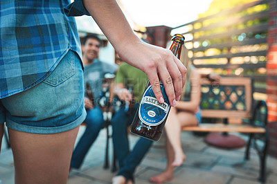 Buy stock photo Closeup shot of a young woman holding a bottle of beer with her friends hanging out in the background