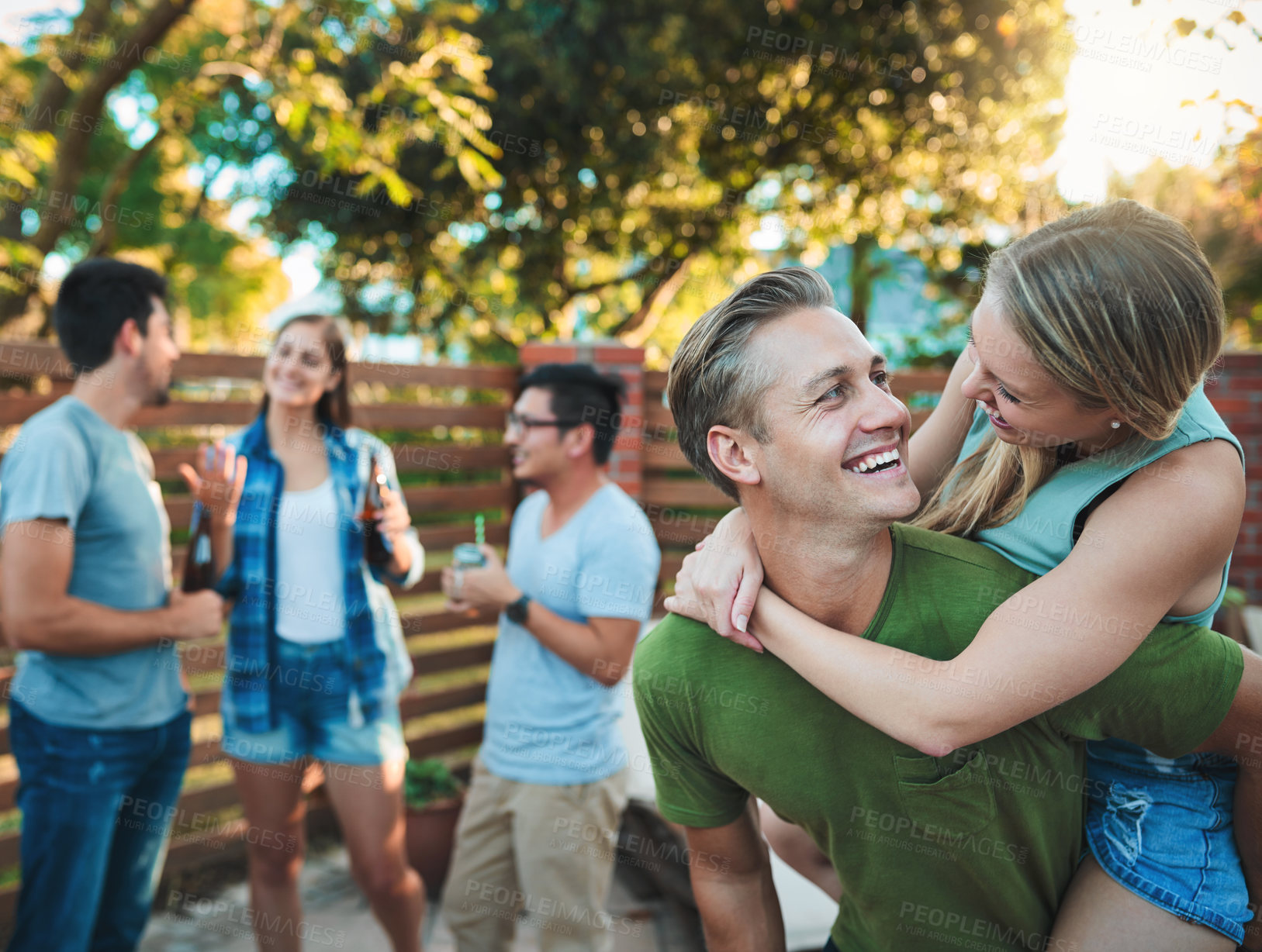 Buy stock photo Couple, hug and patio party backyard with friends, love and outdoor at labor day and social event. Piggy back, conversation and happy people with summer fun, vacation and group with smile and care