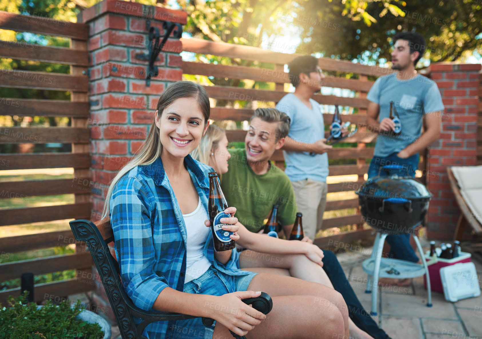 Buy stock photo Shot of a happy young woman enjoying a beer at a barbecue with her friends