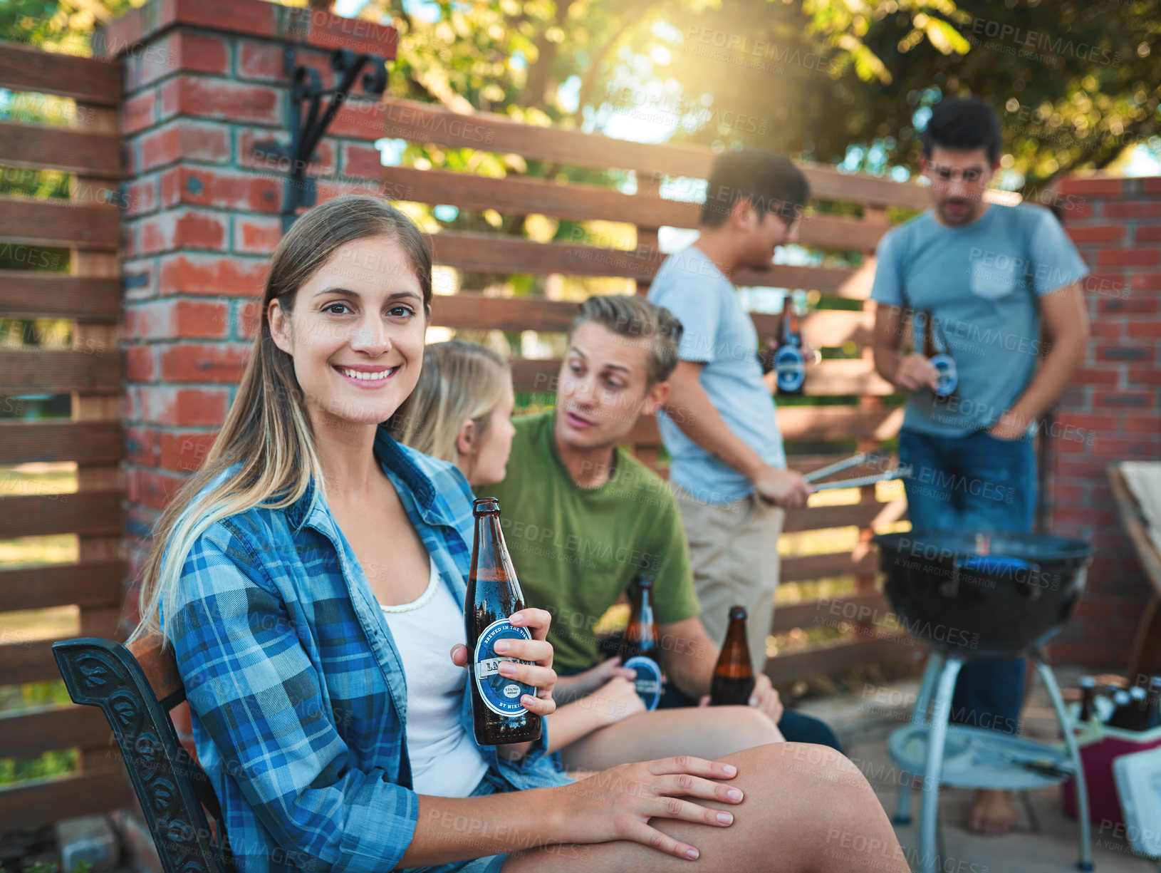 Buy stock photo Shot of a happy young woman enjoying a beer at a barbecue with her friends