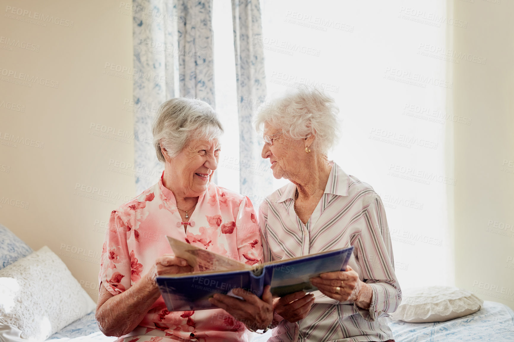Buy stock photo Friends, photo album and happy senior women on bed with memory, photograph or bonding in nursing home. Family tree, conversation and elderly siblings in bedroom with nostalgia, remember or history