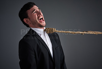 Buy stock photo Studio shot of a young businessman being pulled by a hangman’s noose against a gray background