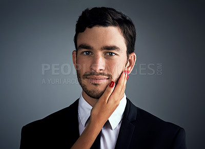 Buy stock photo Studio portrait of a handsome young businessman being touched by an unrecognizable woman’s hand against a gray background