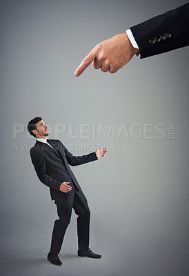 Buy stock photo Studio shot of a young businessman being reprimanded by a giant hand against a gray background