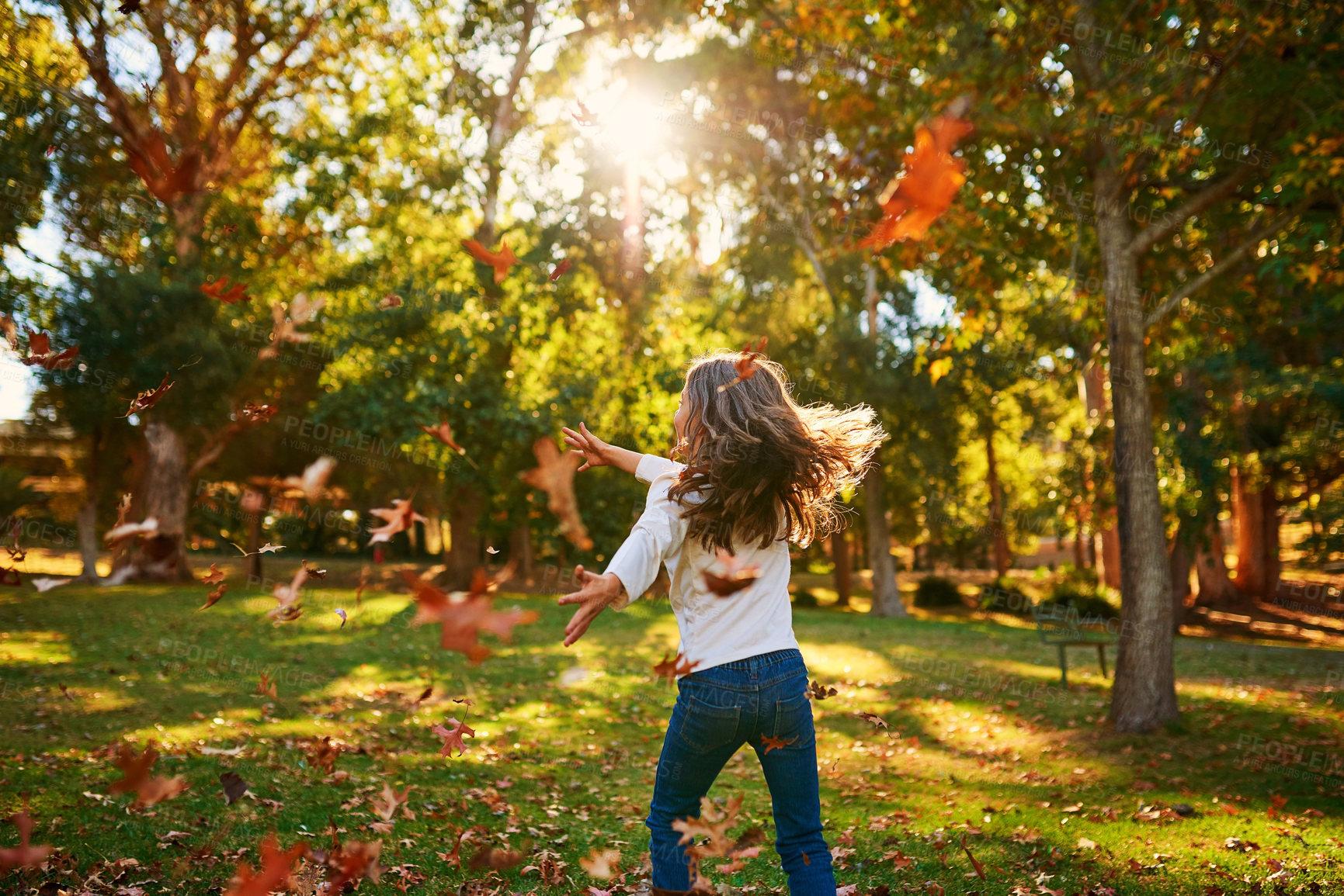 Buy stock photo Girl, kid and playing in park with leaves for adventure, fun activity or spinning with enjoyment in autumn. Child, back and outdoor with freedom, holiday and wellness on grass in nature with sunlight