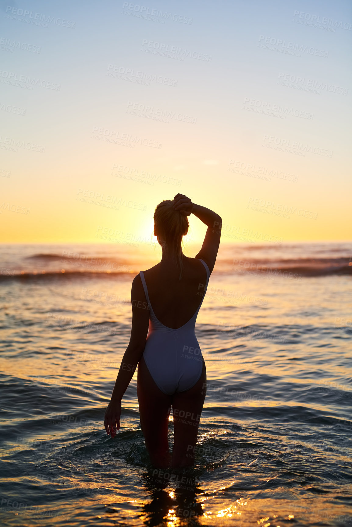 Buy stock photo Rearview shot of a young woman standing in the water at sunset