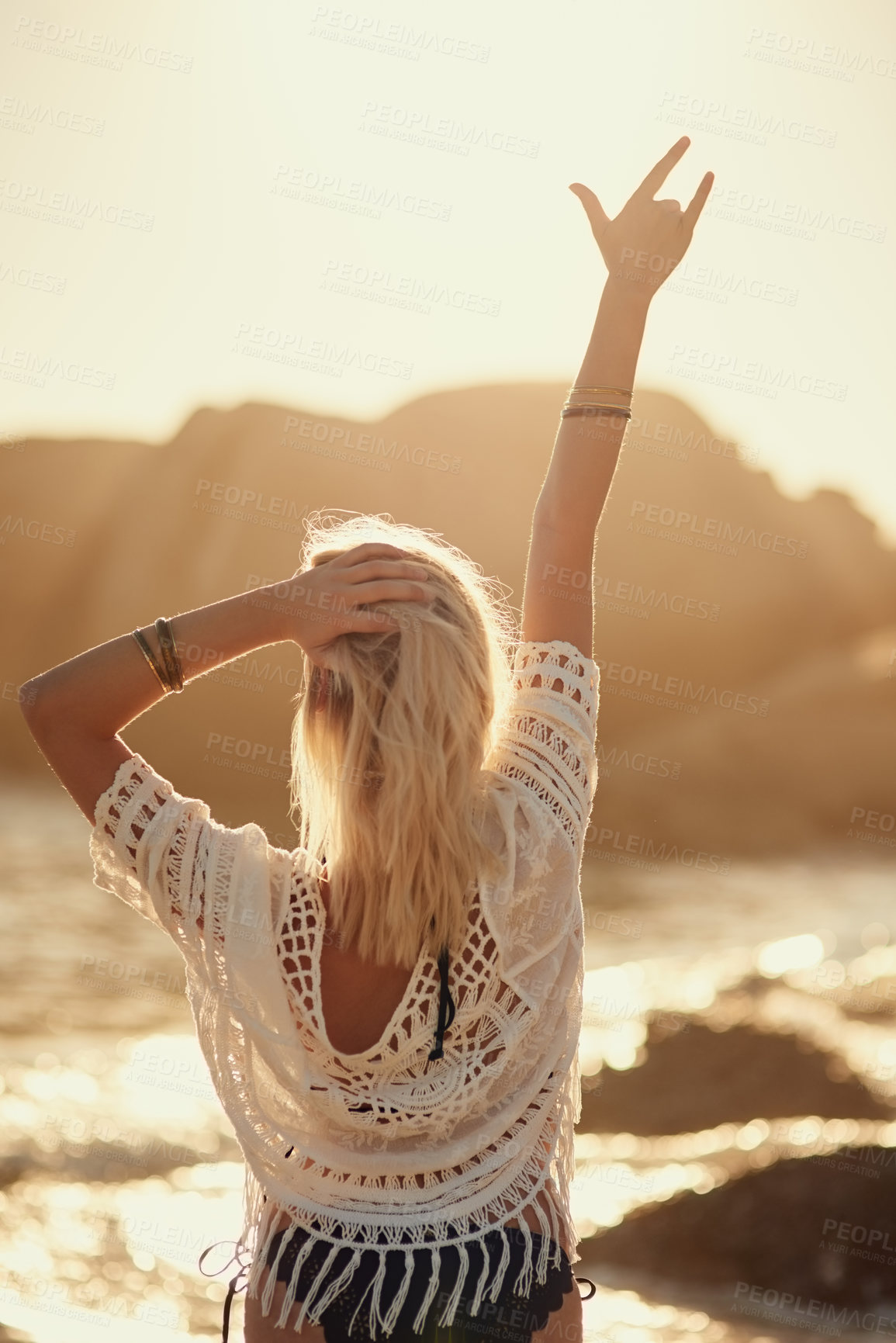 Buy stock photo Rearview shot of a young woman on the beach with her hand in the air