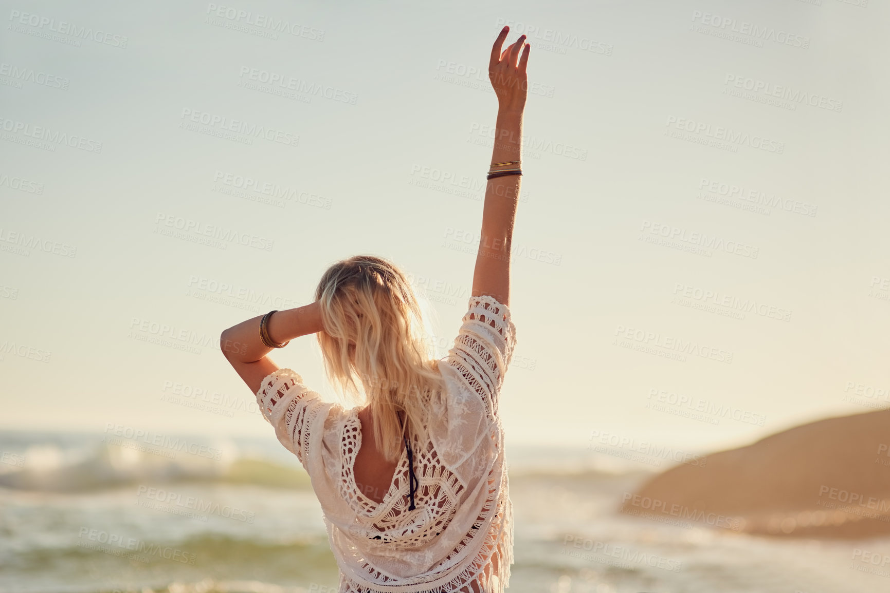 Buy stock photo Rearview shot of a young woman on the beach with her hand in the air