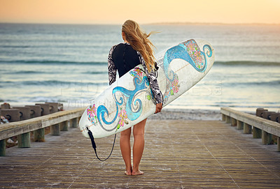 Buy stock photo Rearview shot of an unrecognizable young female surfer standing with her surfboard looking over the ocean