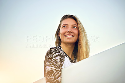Buy stock photo Low angle shot of an attractive young female surfer standing with her surfboard on the beach