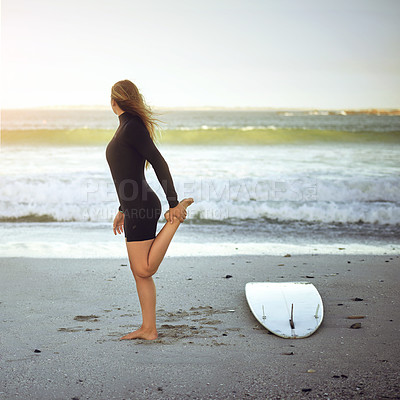 Buy stock photo Full length shot of an unrecognizable young female surfer warming up on the beach