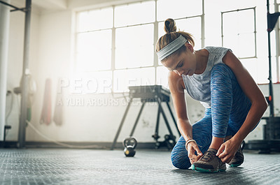 Buy stock photo Shot of a young attractive woman tying her shoelaces in a gym