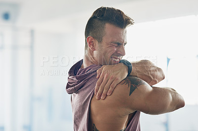 Buy stock photo Shot of a handsome young man stretching at the gym