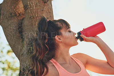 Buy stock photo Cropped shot of a sporty young woman having a sip of water while leaning against a tree