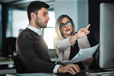 Buy stock photo Shot of two businesspeople looking at something on a desktop while discussing paperwork