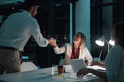 Buy stock photo Shot of a businessman and businesswoman shaking hands during a late night meeting at work