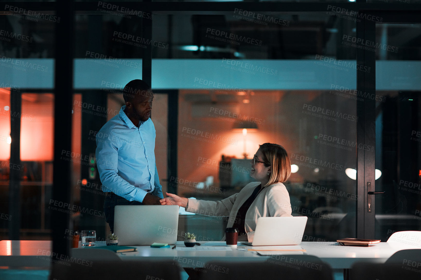 Buy stock photo Handshake, talking and agreement by laptop in office, night and listening for financial advice. Man, woman and teamwork for review deadline or deal with project partnership, dark or decision