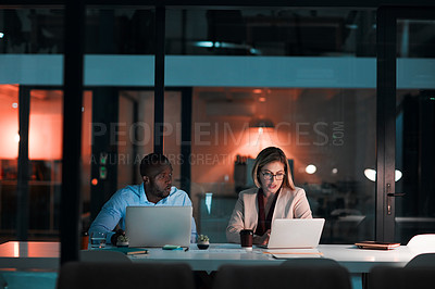 Buy stock photo Shot of two colleagues using their laptops during a late night in a modern office