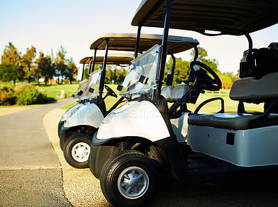 Buy stock photo Shot of three golf carts standing side by side next to a golf course