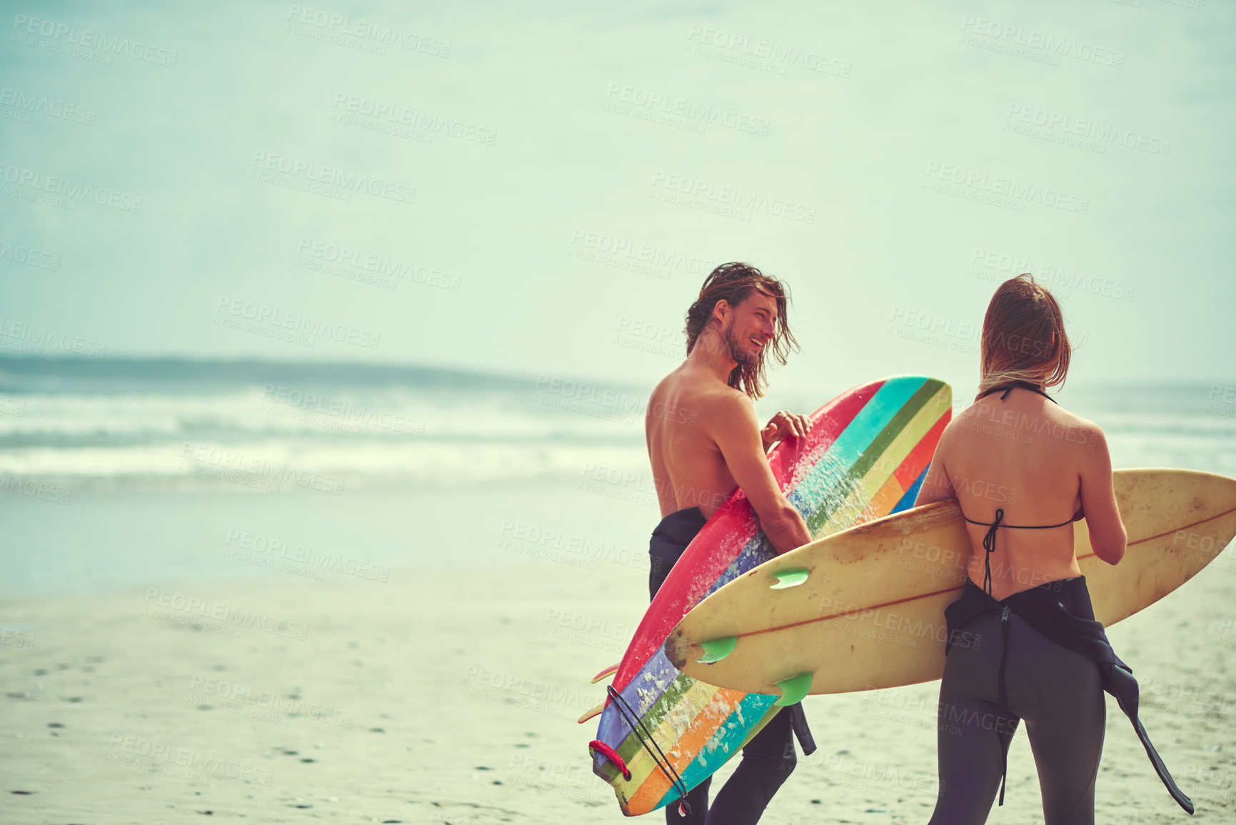 Buy stock photo Shot of a young couple walking on the beach with their surfboards