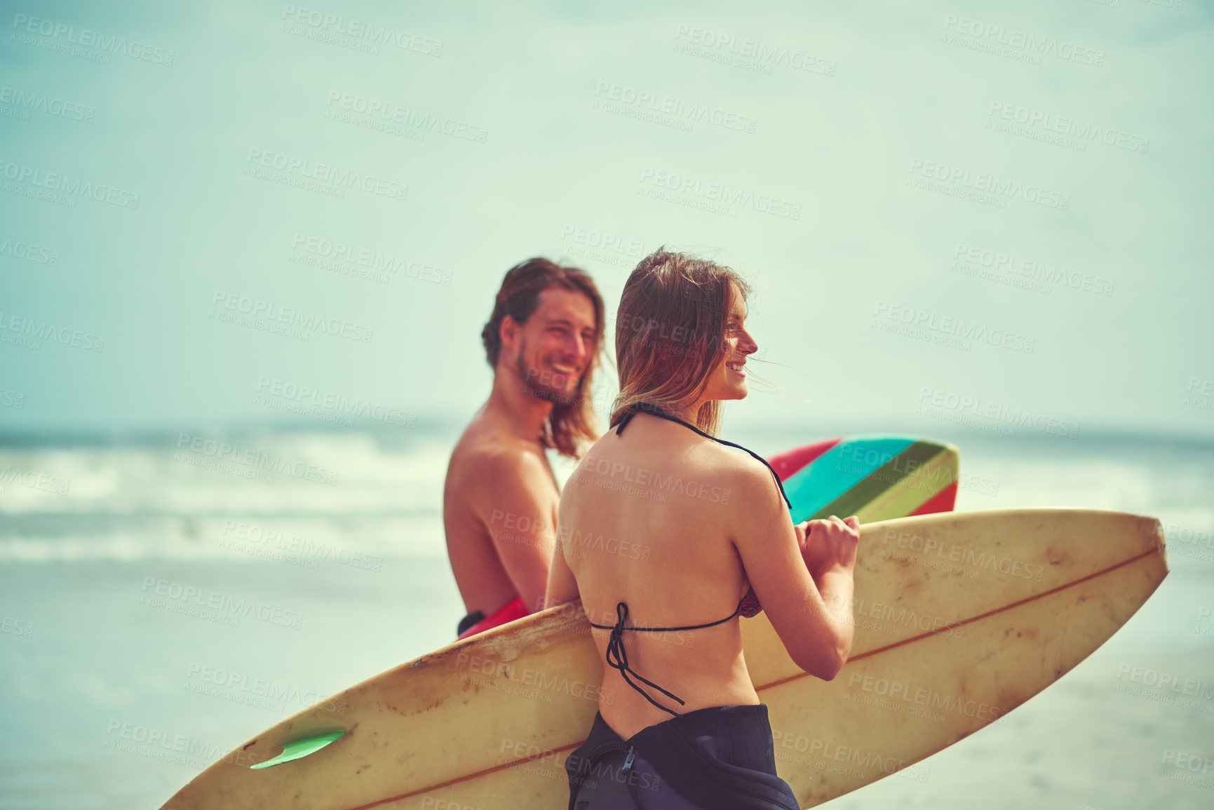 Buy stock photo Shot of a young couple walking on the beach with their surfboards