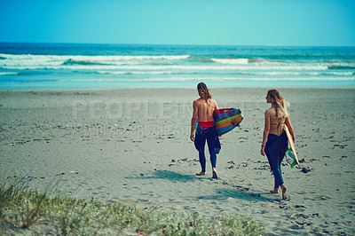 Buy stock photo Shot of a young couple walking on the beach with their surfboards