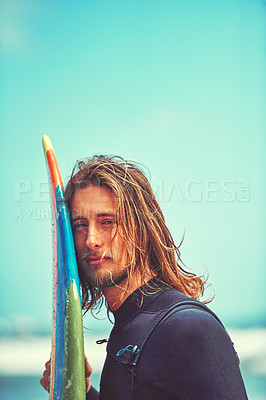 Buy stock photo Cropped shot of a young surfer leaning against his surfboard