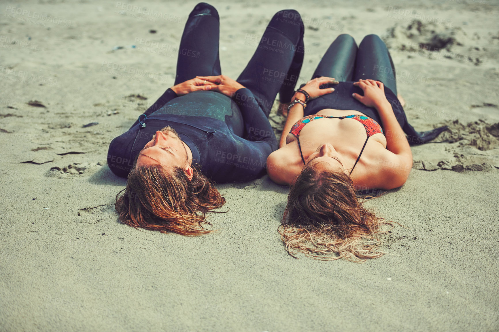 Buy stock photo Shot of a young couple relaxing after a surf at the beach