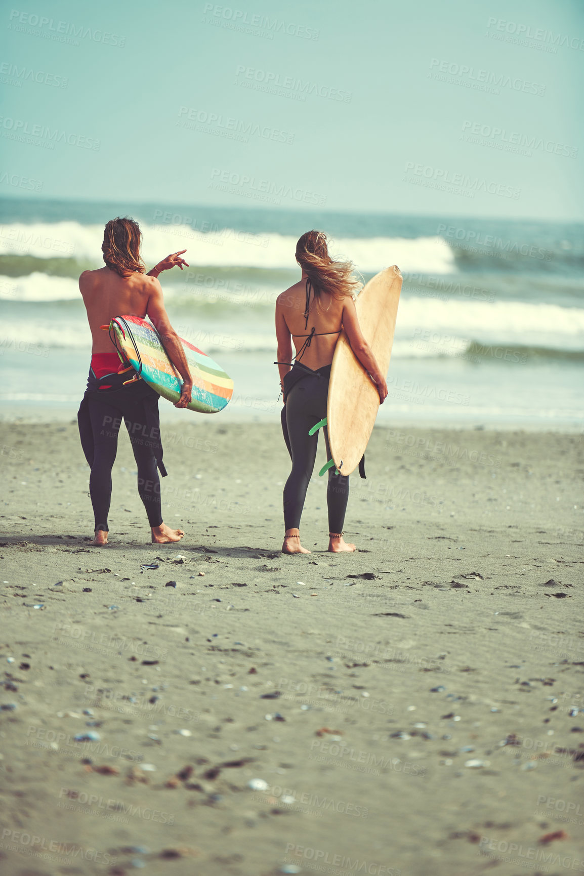 Buy stock photo Shot of a young couple walking on the beach with their surfboards