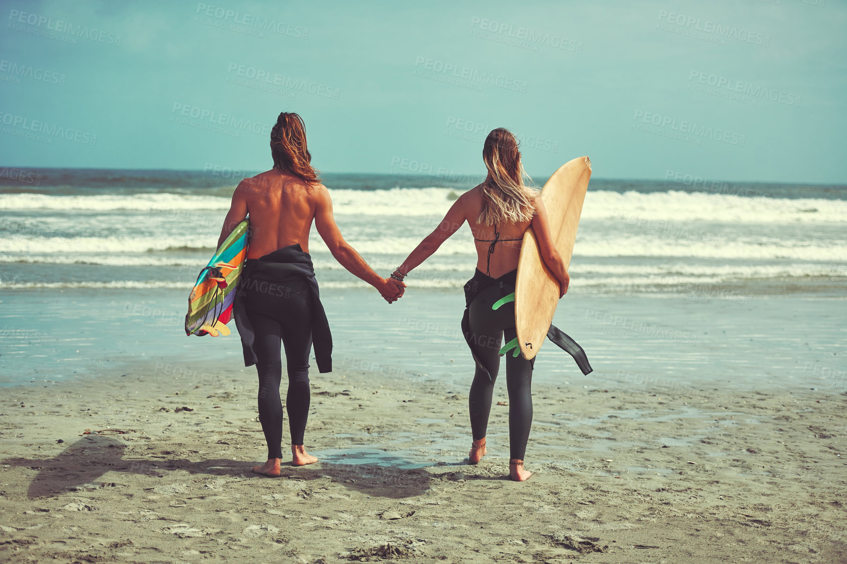 Buy stock photo Shot of a young couple walking on the beach with their surfboards