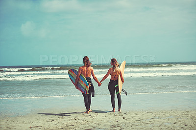 Buy stock photo Shot of a young couple walking on the beach with their surfboards