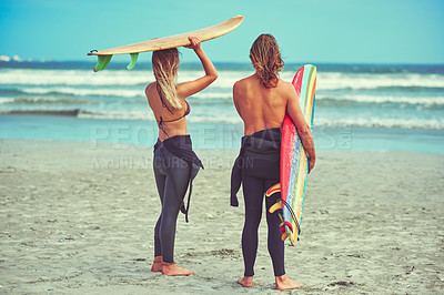 Buy stock photo Shot of a young couple walking on the beach with their surfboards