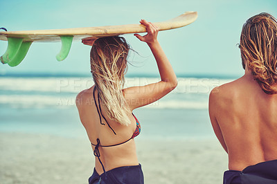 Buy stock photo Shot of a young couple walking on the beach with their surfboards