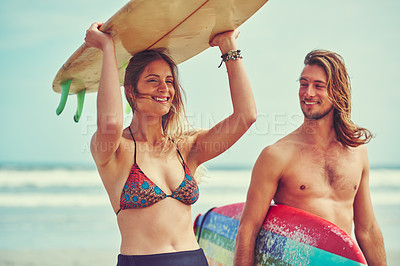 Buy stock photo Shot of a young couple walking on the beach with their surfboards